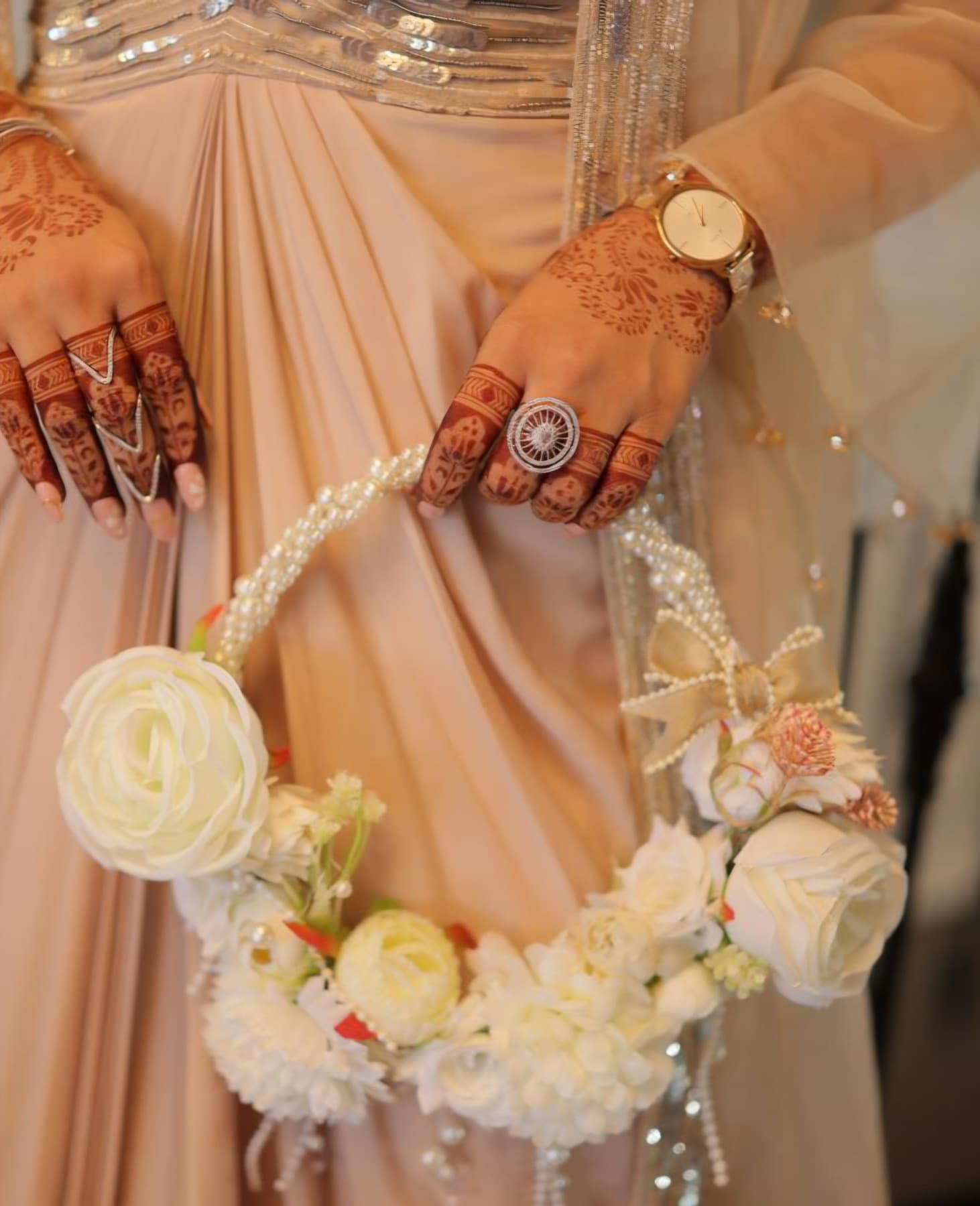 A guest in a peach saree carrying a white rose and pearl purse bouquet